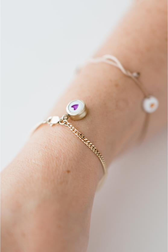 A close-up of Veerle Peeters' arm with 2 bracelets, one with an orange heart in the back and a golden one with a purple heart in front